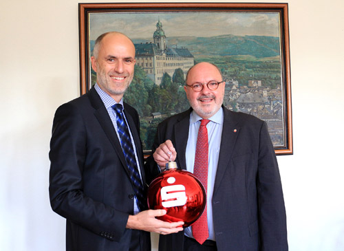 Carsten Sprenger, Vorstand der Kreissparkasse Saalfeld-Rudolstadt, überreicht Bürgermeister Jörg Reichl eine der 80 Weihnachtskugeln, die in diesem Jahr erstmals den Weihnachtsmarkt vor dem Rathaus in Rudolstadt schmücken werden. Foto: Tom Demuth