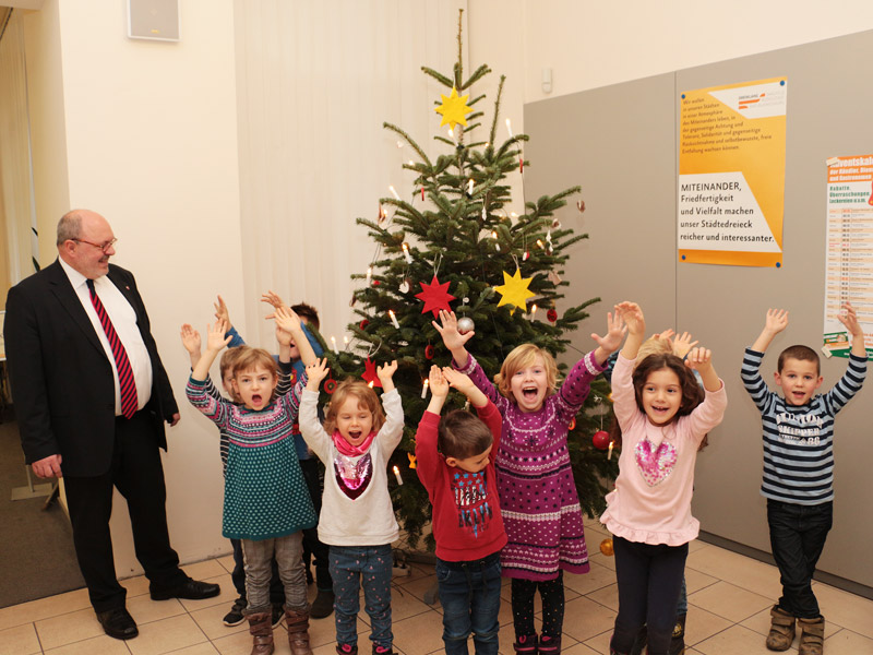 Bürgermeister Jörg Reichl und die Kinder aus dem Kindergarten Baum des Lebens freuen sich über den bunt geschmückten Weihnachtsbaum im Bürgerservice. Foto: Tom Demuth