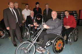 Im Vordergrund Olaf Schnabelrauch, an dessen Rollstuhl das Handbike zu Demonstrationszwecken montiert wurde, im Hintergrund auf den weiteren Rollstühlen links Dr. Brockhausen und rechts der Vertreter der Herstellerfirma Speedy, Knut Matz sowie die weiteren Sponsoren und ihre Vertreter. 